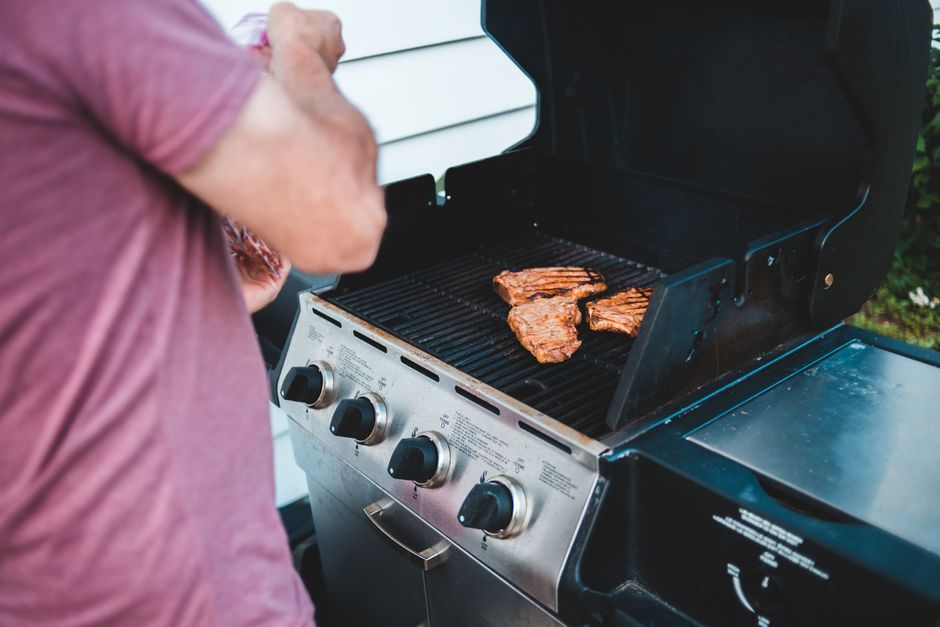 Man grilling steaks on an outdoor gas barbecue, showcasing delicious food preparation.